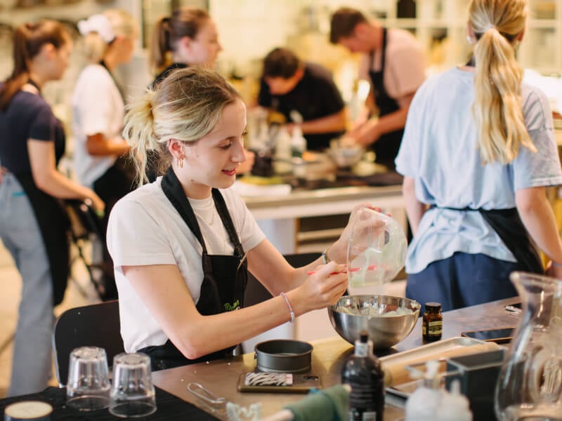 Young woman adding ingredients to a bowl in an industrial kitchen